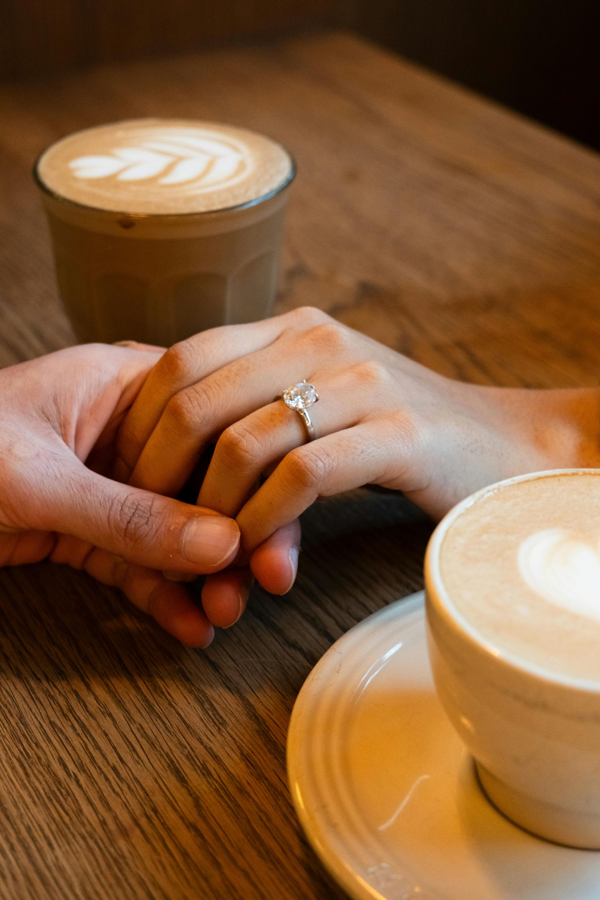 A man and woman are holding hands at a table with a cup of coffee.