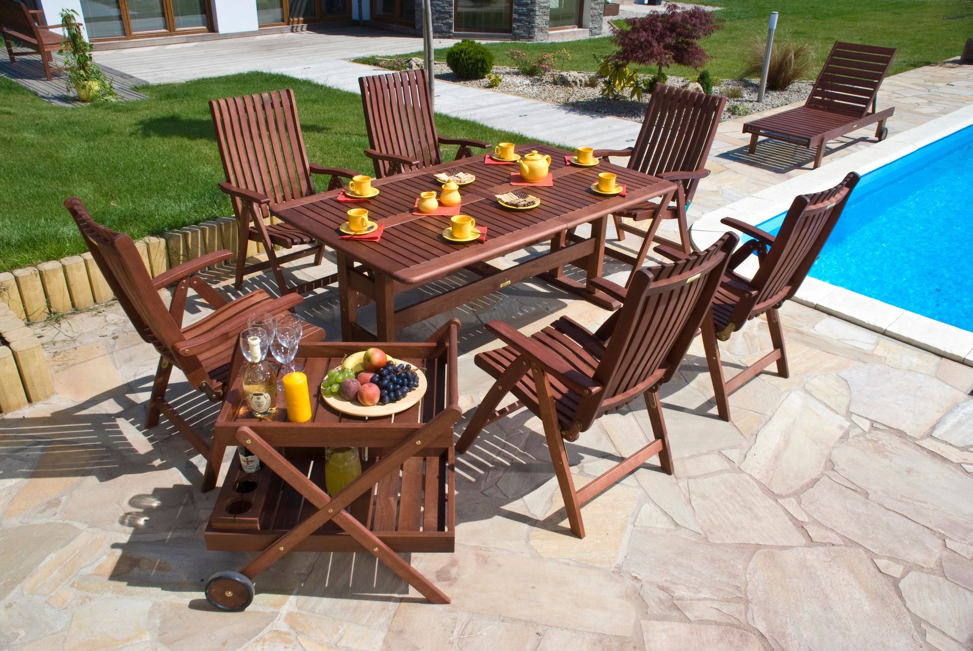 Tavolo da pranzo all'aperto vicino alla piscina: tavolo e sedie in legno, cibo, bevande, giornata di sole.