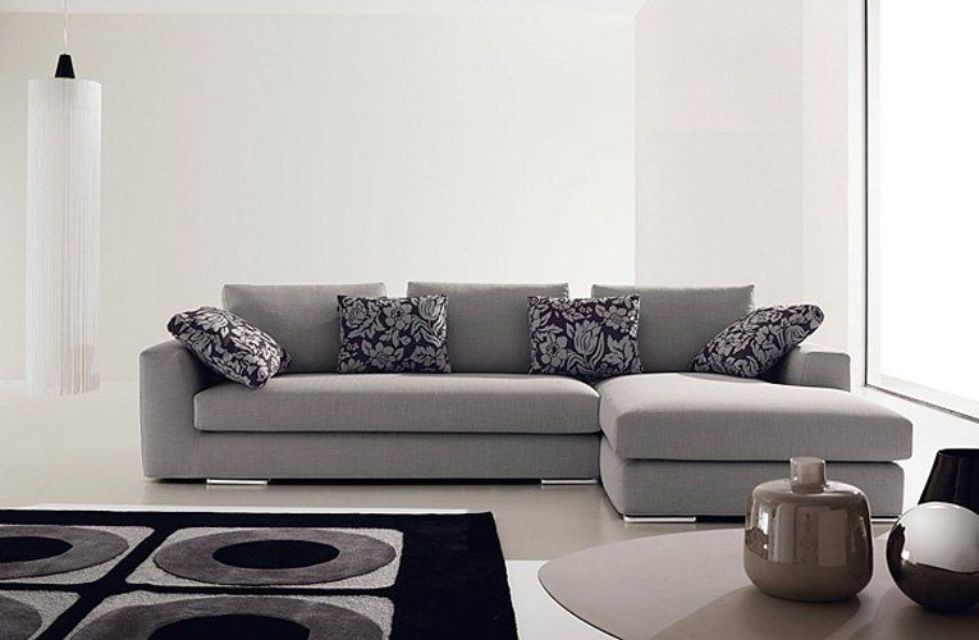 Divano componibile grigio con cuscini fantasia in una moderna stanza bianca.