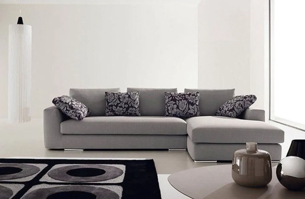 Divano componibile moderno grigio con cuscini fantasia in una stanza bianca.