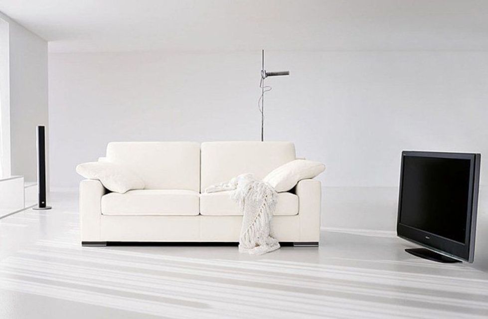 Soggiorno bianco con divano, TV e lampada da terra.