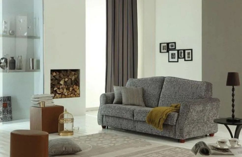 Soggiorno con divano grigio, tavolino, pouf marrone, gabbia decorativa per uccelli e camino.