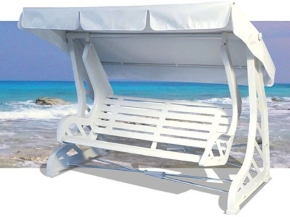 Altalena bianca da esterno con baldacchino, sullo sfondo sfocato di spiaggia e oceano.
