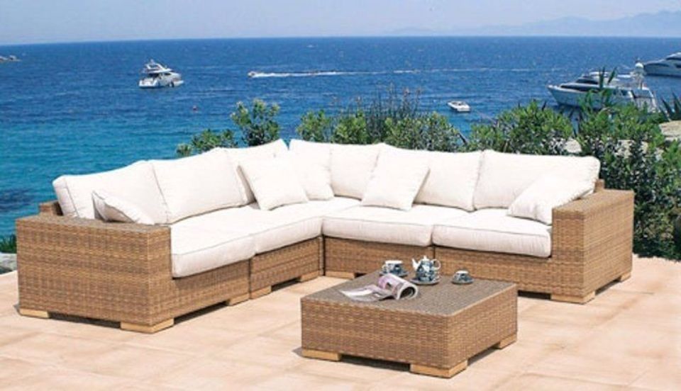 Divano da giardino in vimini a forma di L con cuscini color crema e tavolino da caffè con vista sull'oceano.