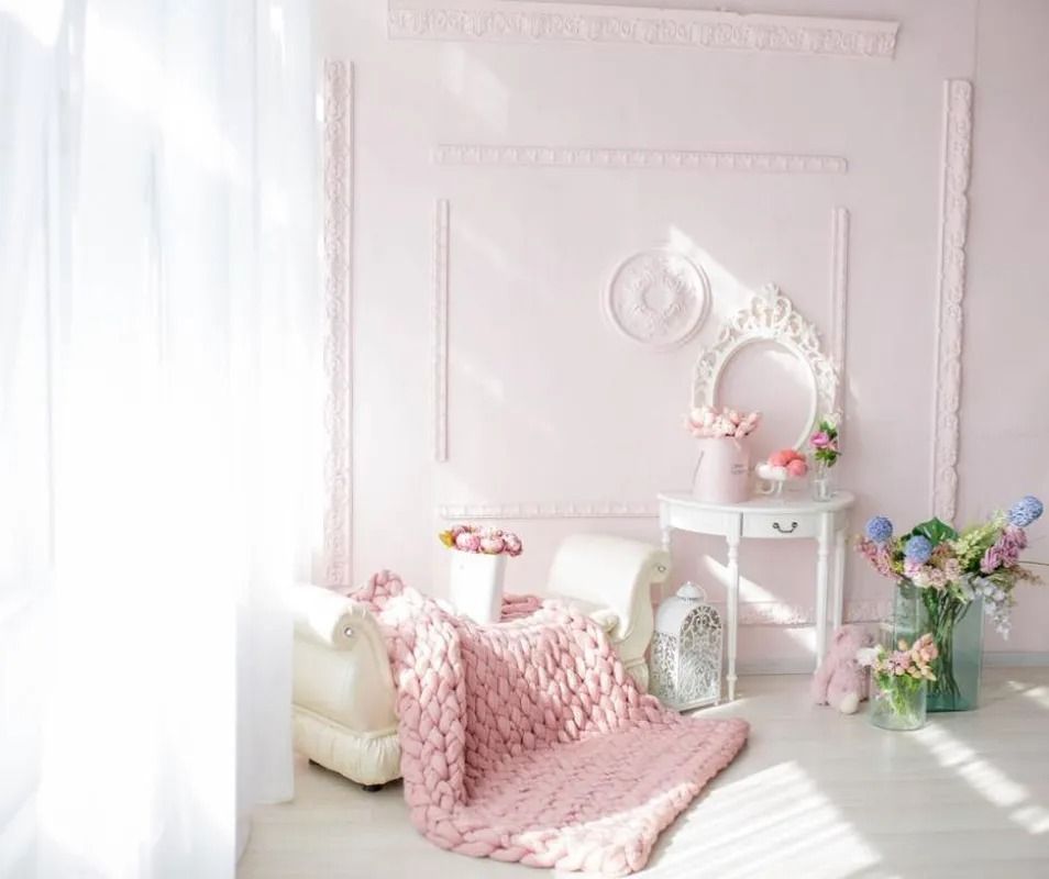 Camera a tema rosa con una coperta di maglia spessa su una sedia, fiori e modanature decorative.