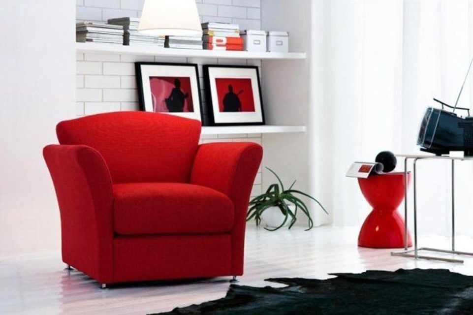 Poltrona rossa in un moderno interno bianco con opere d'arte e tavolino laterale.