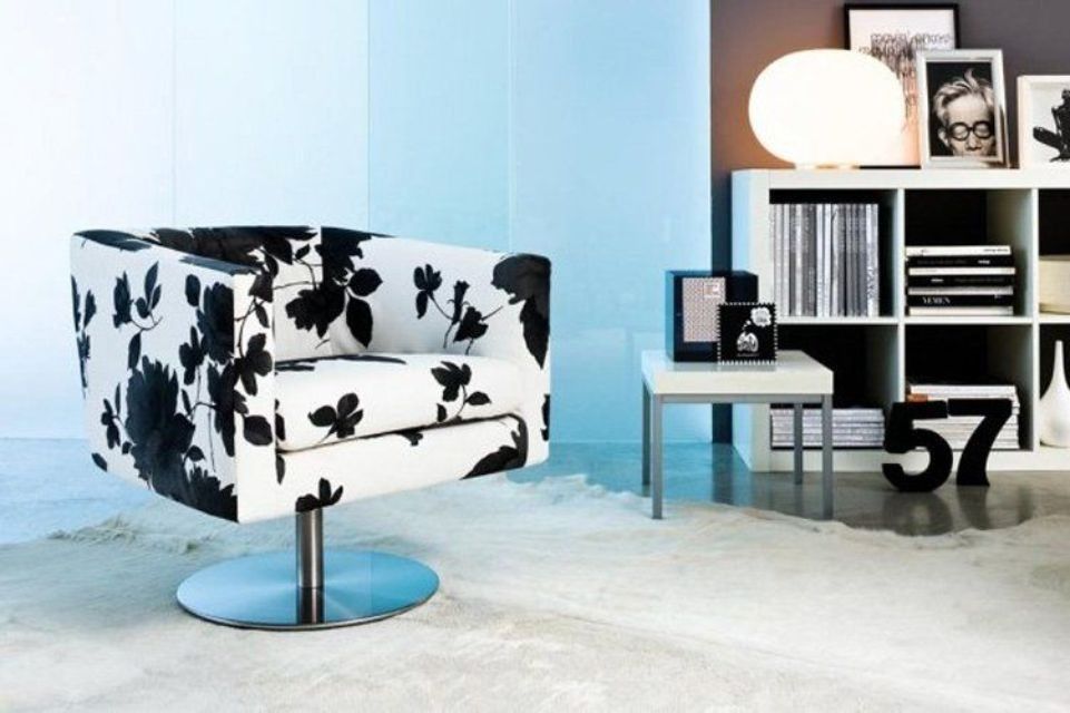 Poltrona girevole con stampa floreale nera, accanto a un tavolino laterale e a un cubo contenitore.