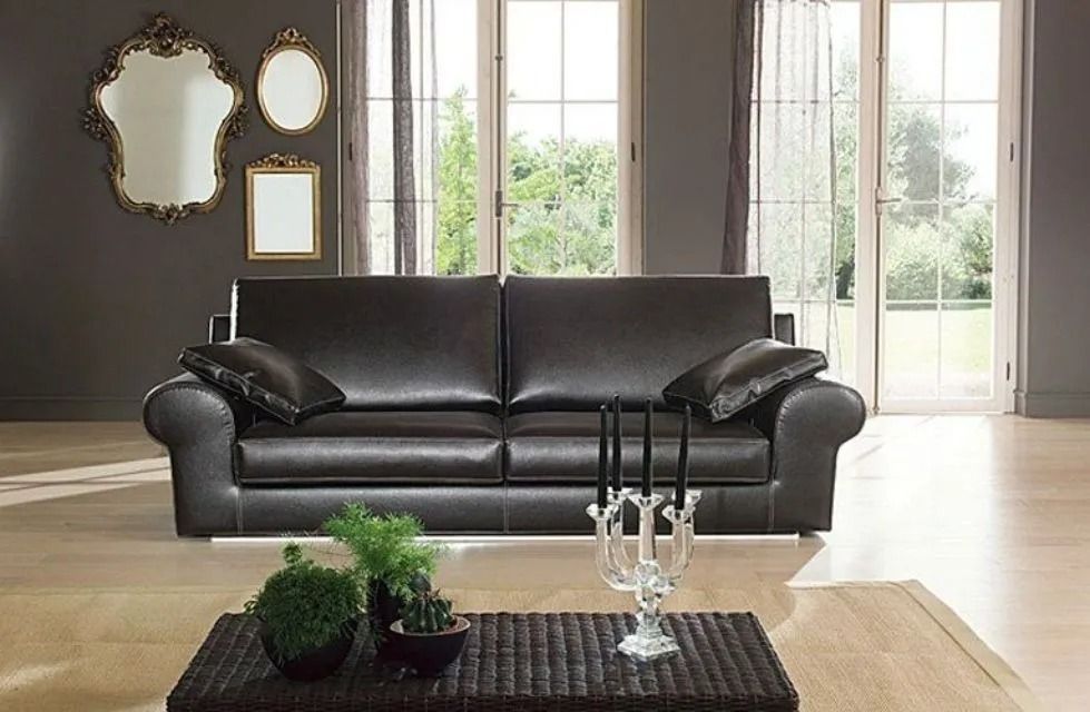 Divano in pelle in una stanza con specchi, tavolino da caffè e ampie finestre.