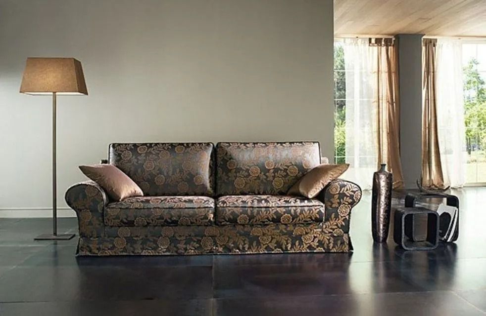 Divano marrone con motivo floreale in un soggiorno moderno con lampada da terra, finestre e pavimento scuro.