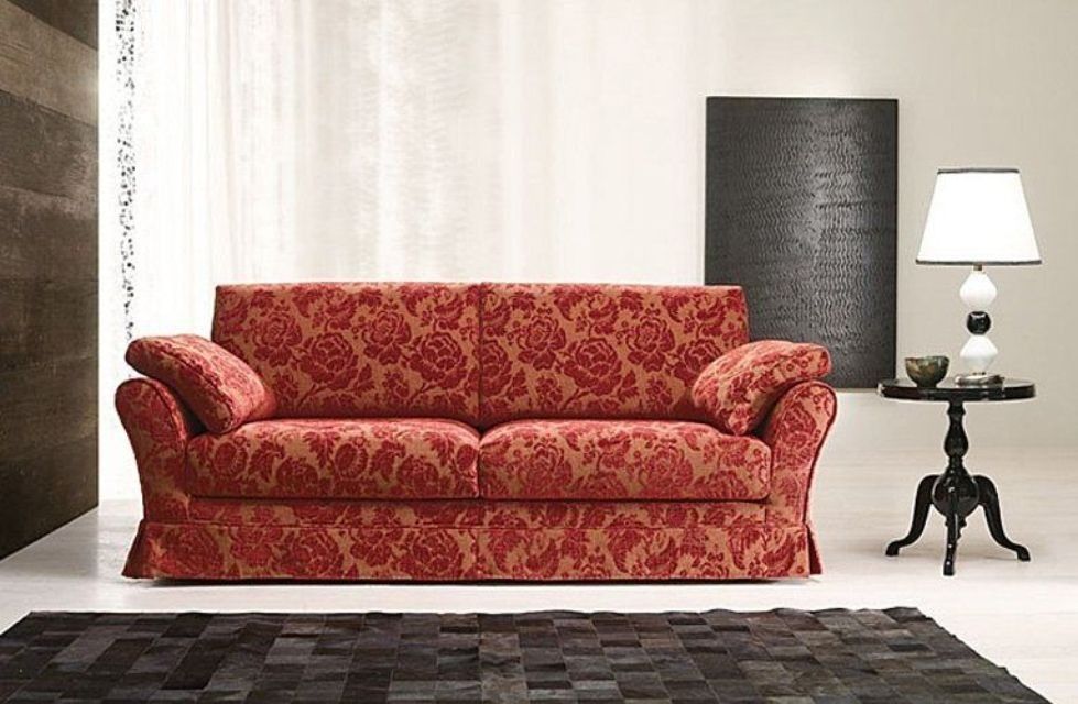 Divano rosso con motivo floreale in un ambiente soggiorno, accanto a un tavolino nero e una lampada.