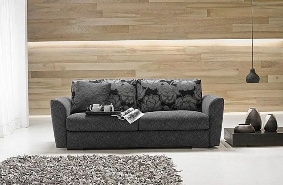 Divano grigio con cuscini floreali contro una parete rivestita in legno, con decorazioni e tappeto.