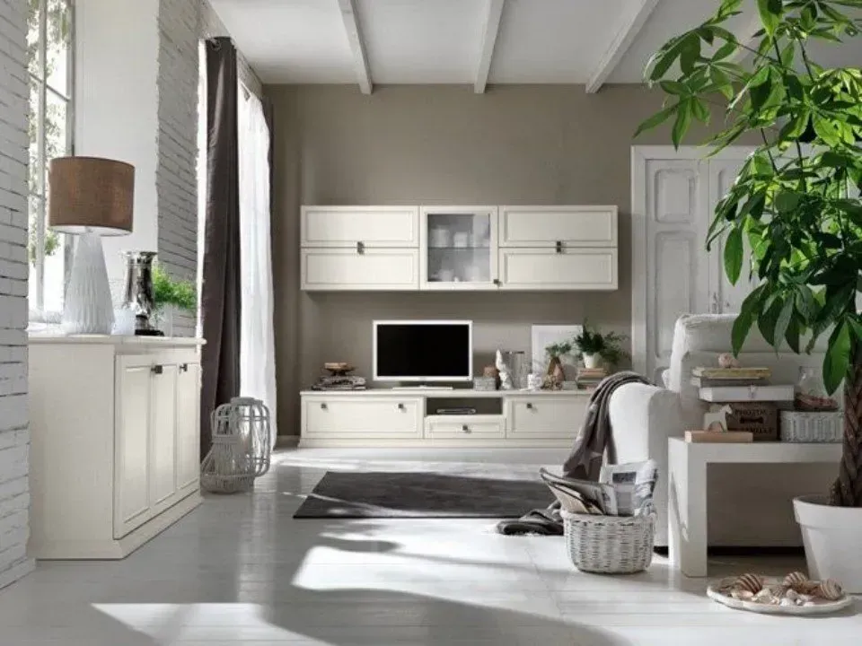 Soggiorno color crema con TV, mobili e una pianta verde in vaso accanto a una finestra.