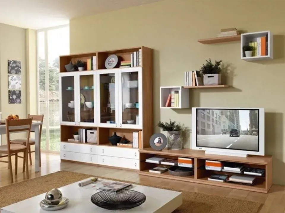 Soggiorno con mobili in legno chiaro e bianchi, tra cui un mobile TV e mensole espositive, contro una parete beige.