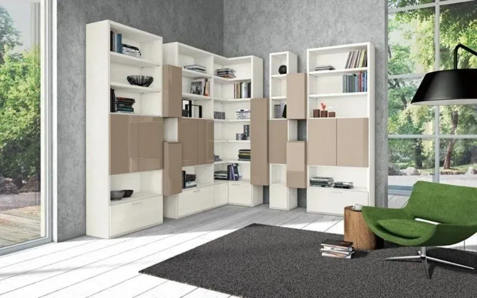 Moderne librerie bianche e beige in un angolo, con libri e decorazioni, vicino a una sedia verde e a una finestra.