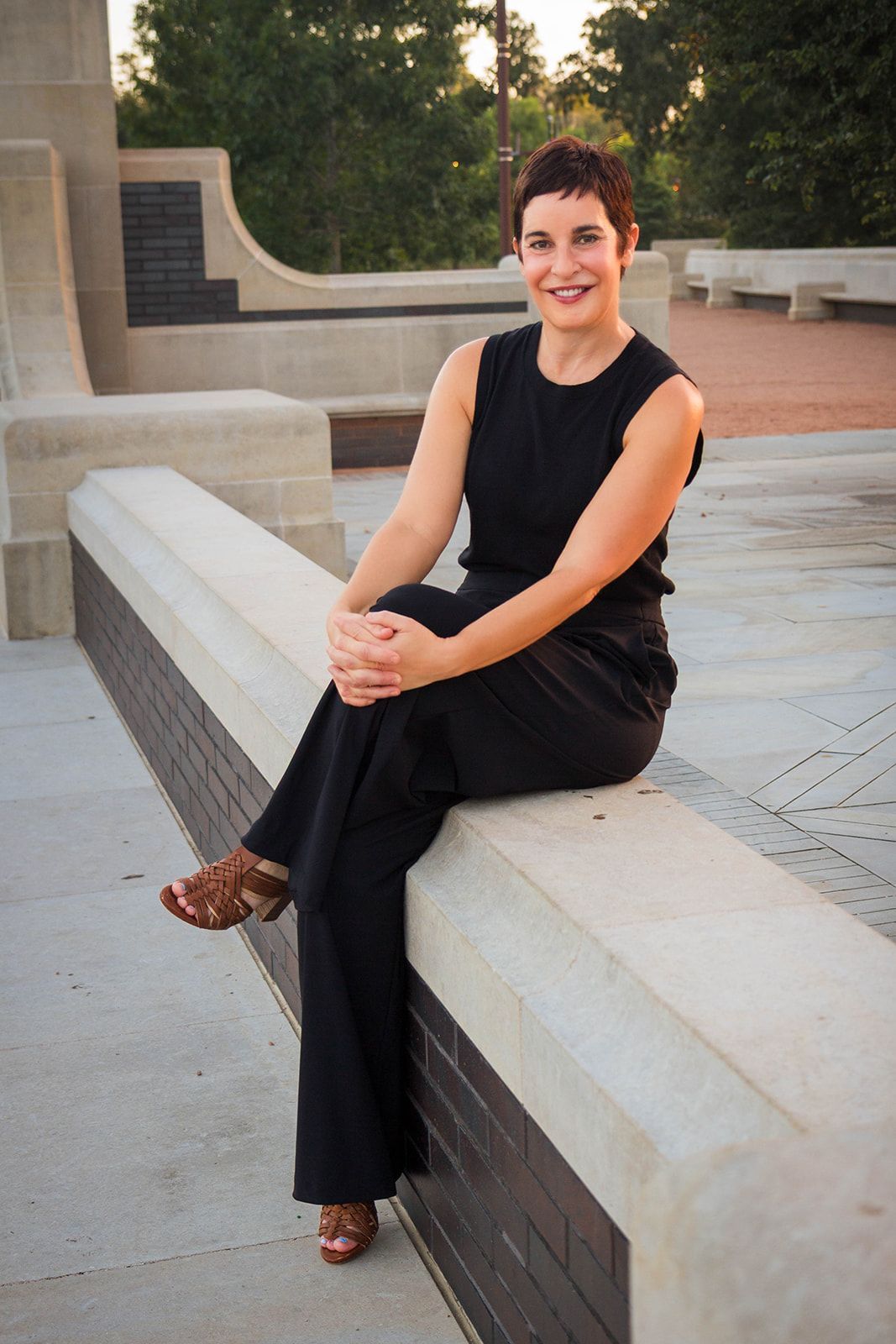A woman is sitting in a chair with her hands folded and smiling