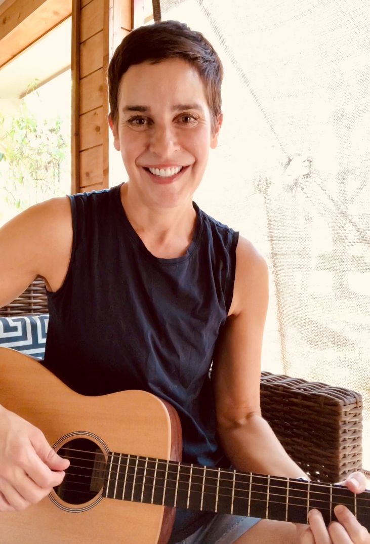 A woman in a black tank top is playing an acoustic guitar
