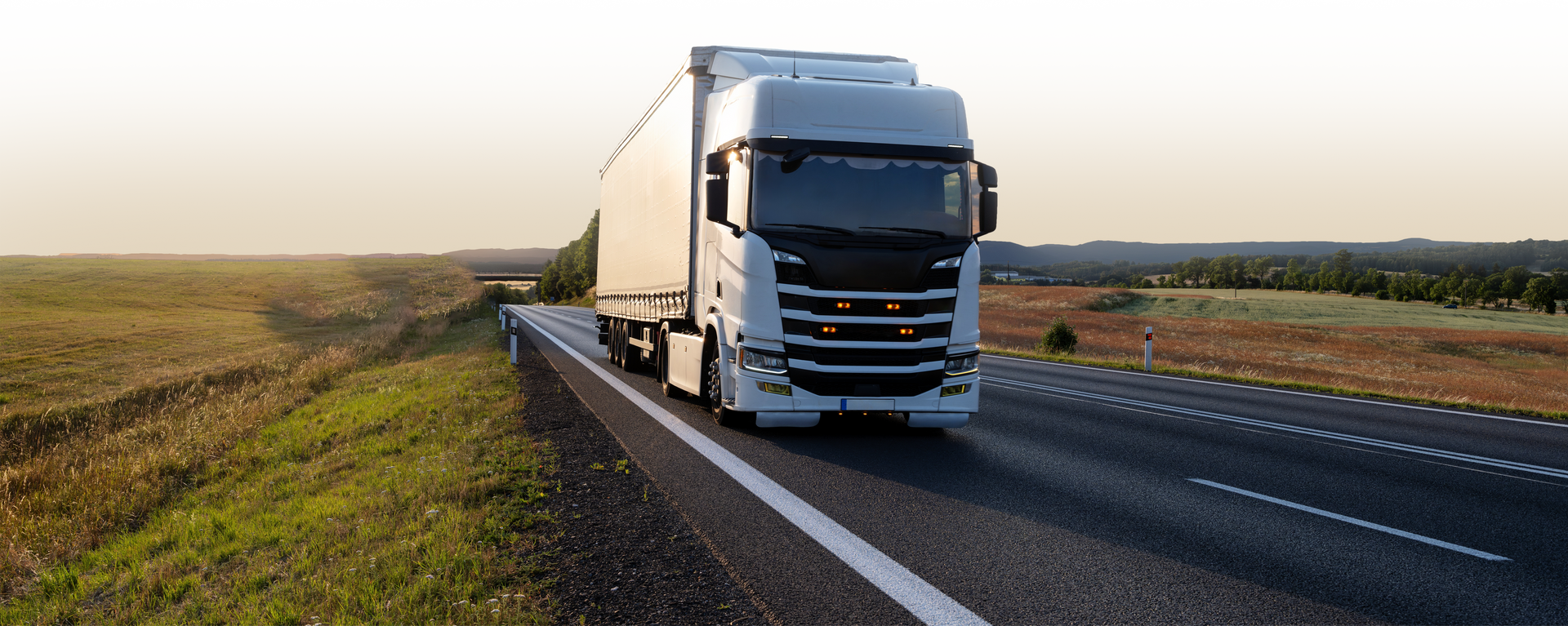 White semi-truck driving on a highway with a green field on the side.