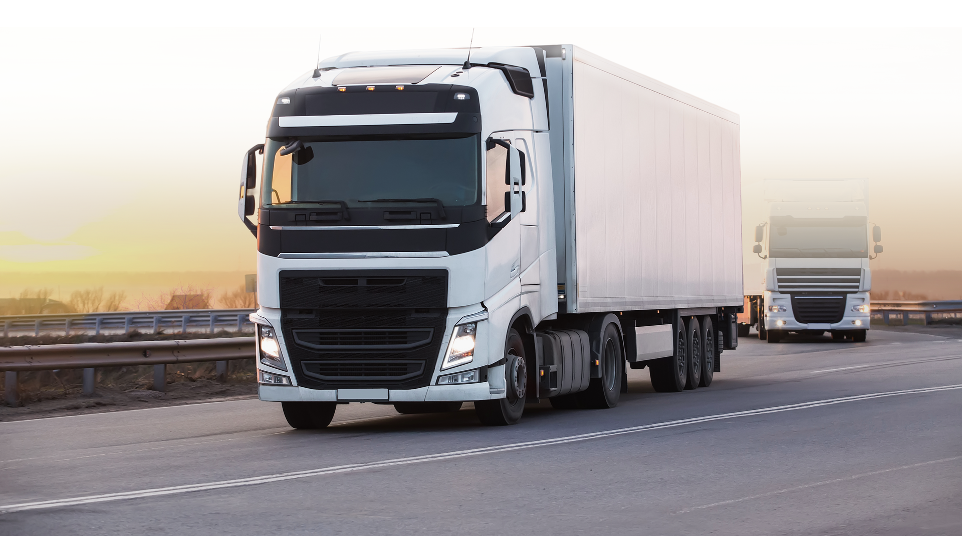 Two white semi-trucks driving on a highway.