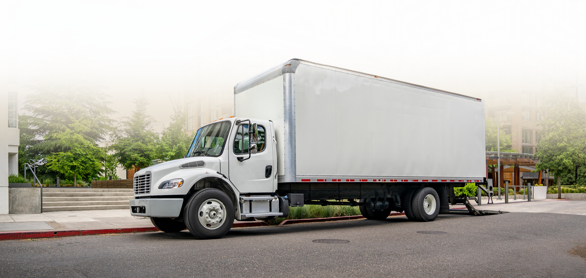 A white box truck parked on a street, next to a sidewalk and building.