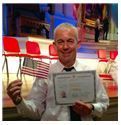 A man in a suit and tie is holding an american flag and a certificate.