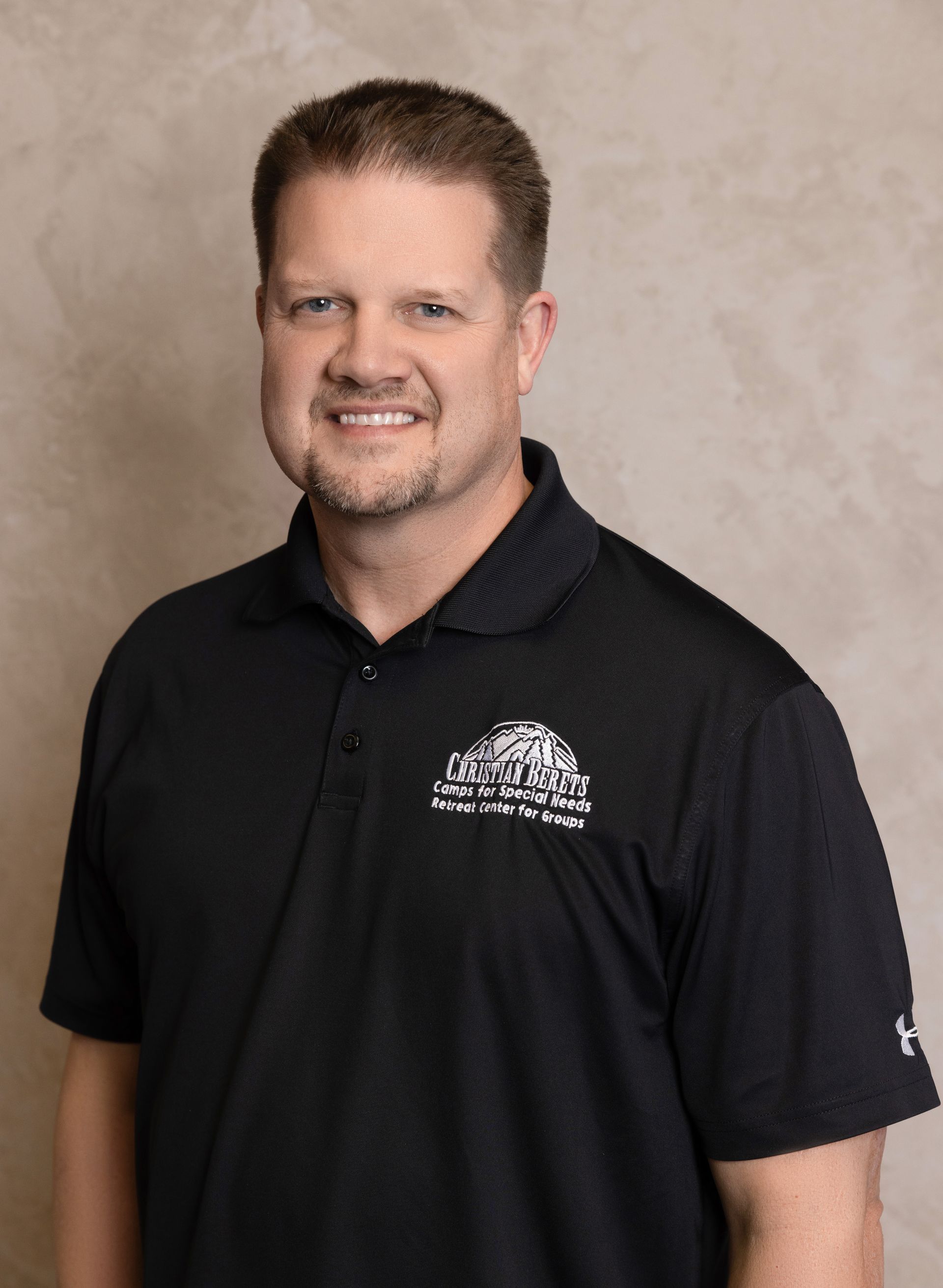 A man wearing a black polo shirt is smiling for the camera.