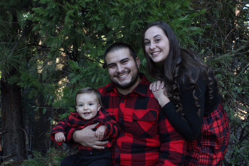 A man , woman and baby are posing for a picture in the woods.