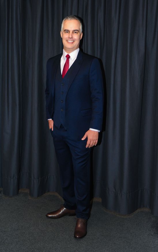 um homem de terno e gravata está parado em frente a uma cortina preta.