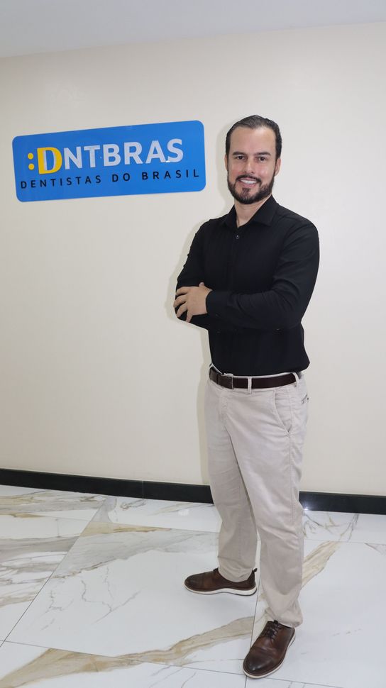 um homem de terno e gravata está parado em frente a uma cortina preta.