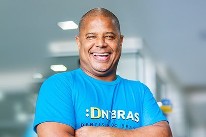 um homem de camisa azul está sorrindo com os braços cruzados.