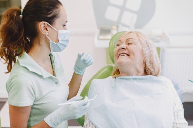 uma mulher está sentada em uma cadeira odontológica conversando com um dentista.