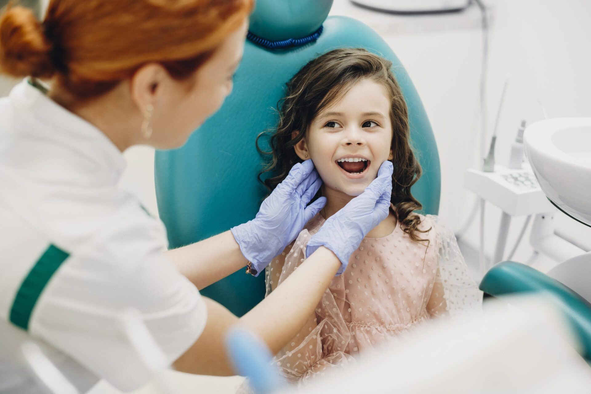 uma menina está sentada em uma cadeira odontológica enquanto um dentista examina seus dentes.