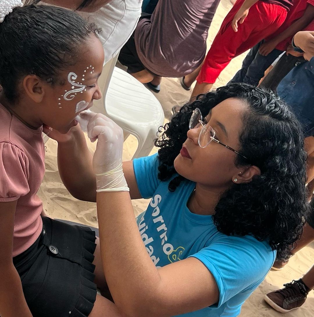 uma mulher de camisa azul está pintando o rosto de uma menina.