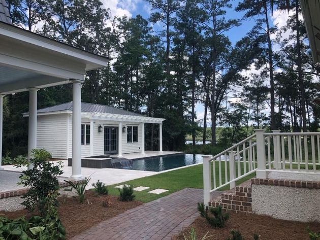 Backyard patio with pool, white house, and screened porch beside a brick path and green lawn