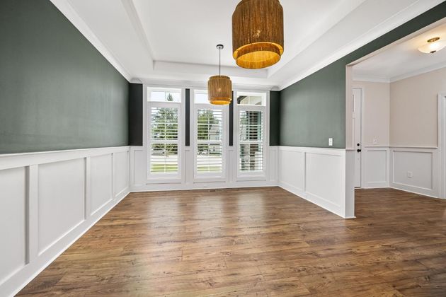Empty dining room with wood floors, green walls, white wainscoting, and hanging woven pendant lights