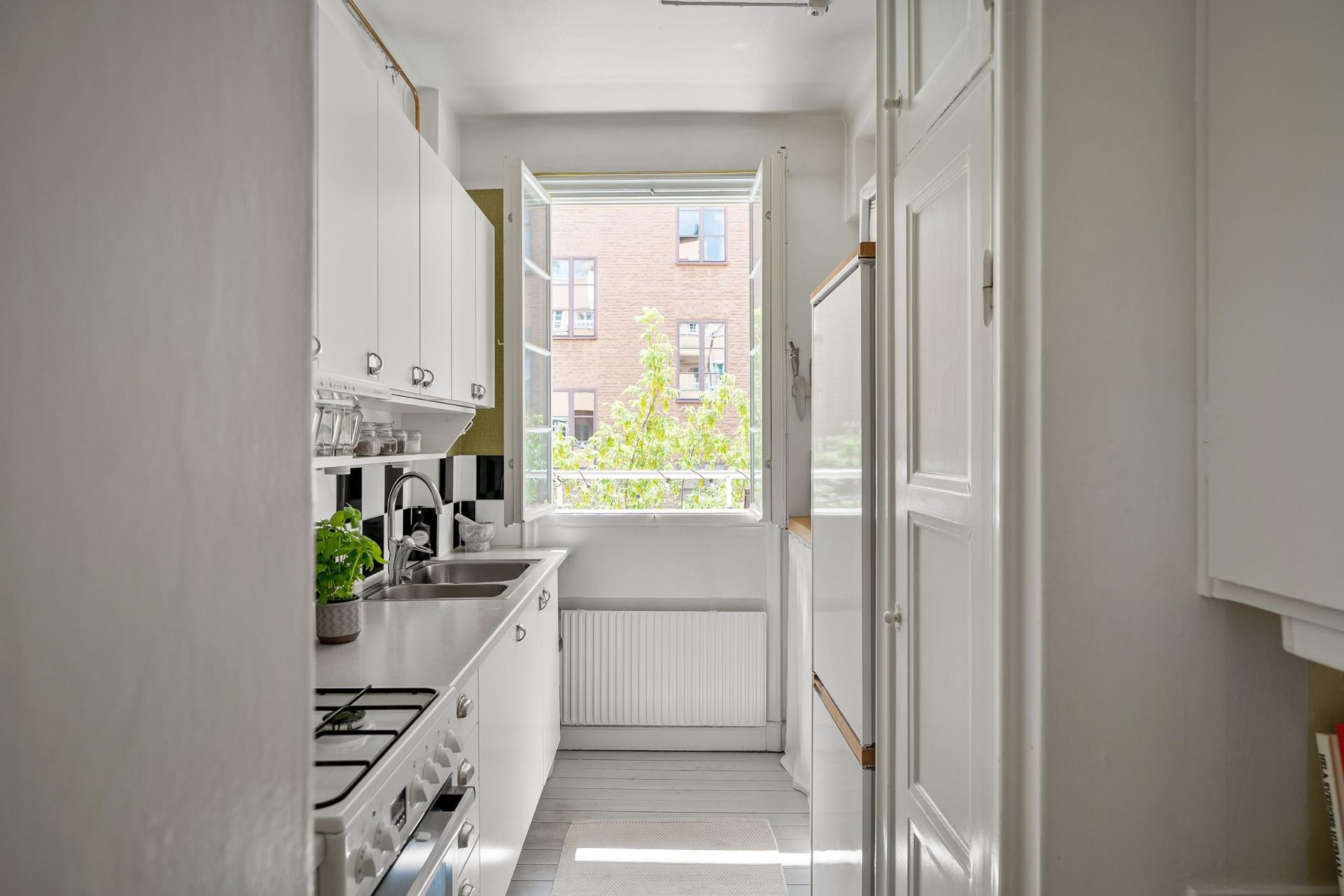 Narrow white kitchen hallway with cabinets, stove, and a bright window at the end