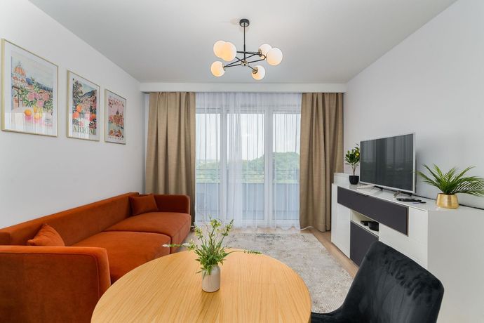 Modern living room with orange sofa, round table, fireplace, and large window with beige curtains.