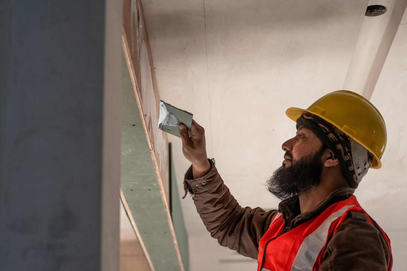 Construction worker in hard hat and red vest inspecting a ceiling with a handheld device