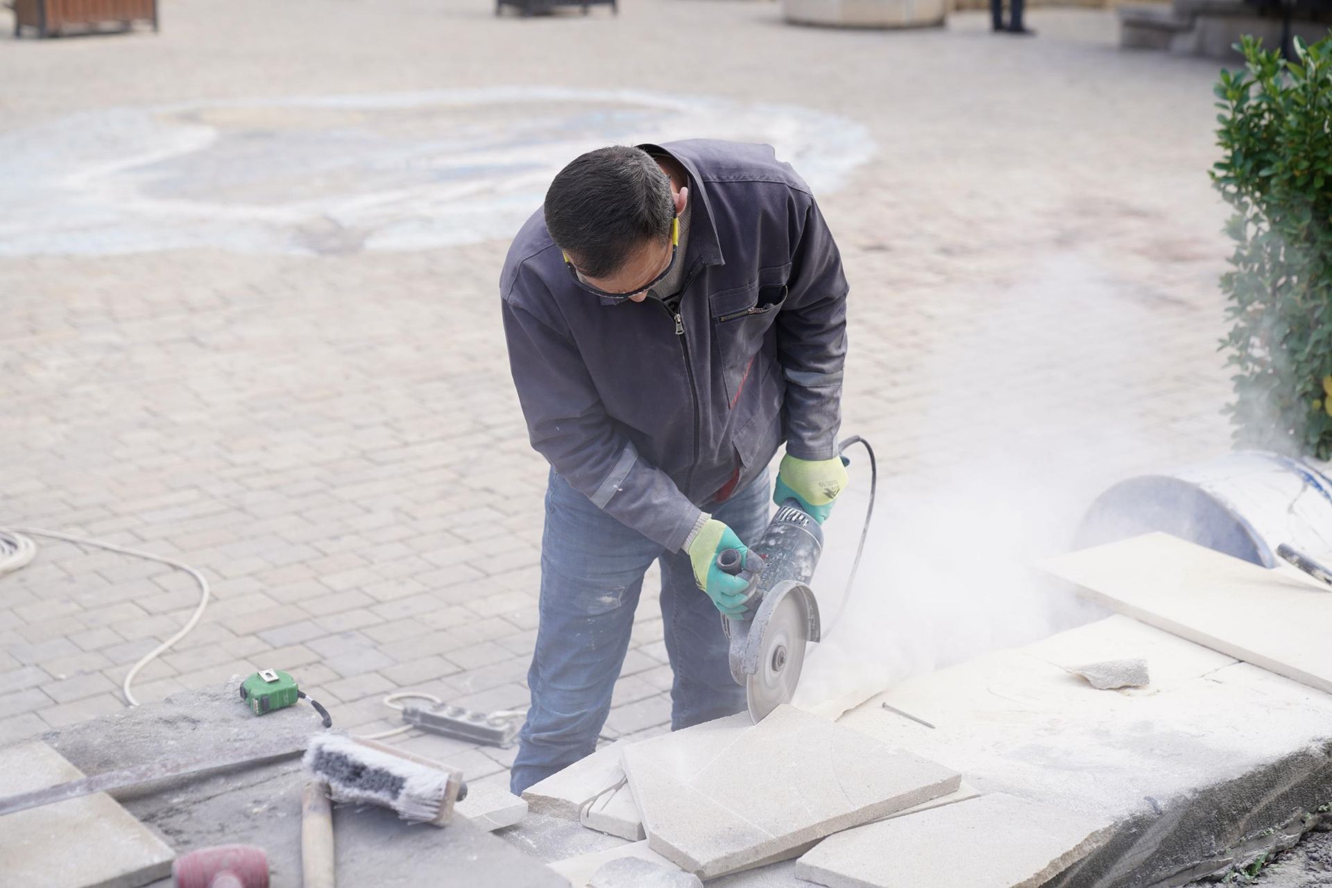 Worker using a circular saw to cut a concrete slab outdoors, with dust and debris around him