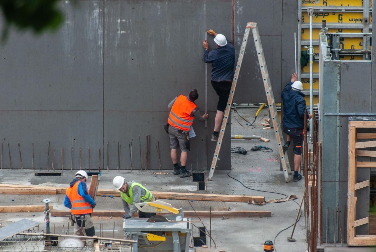 Construction workers on scaffolding and ladders applying finish to a concrete wall.
