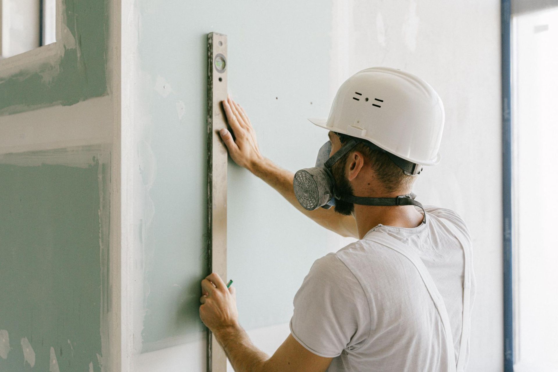 Worker in white hard hat measuring a wall with a level during interior renovation.