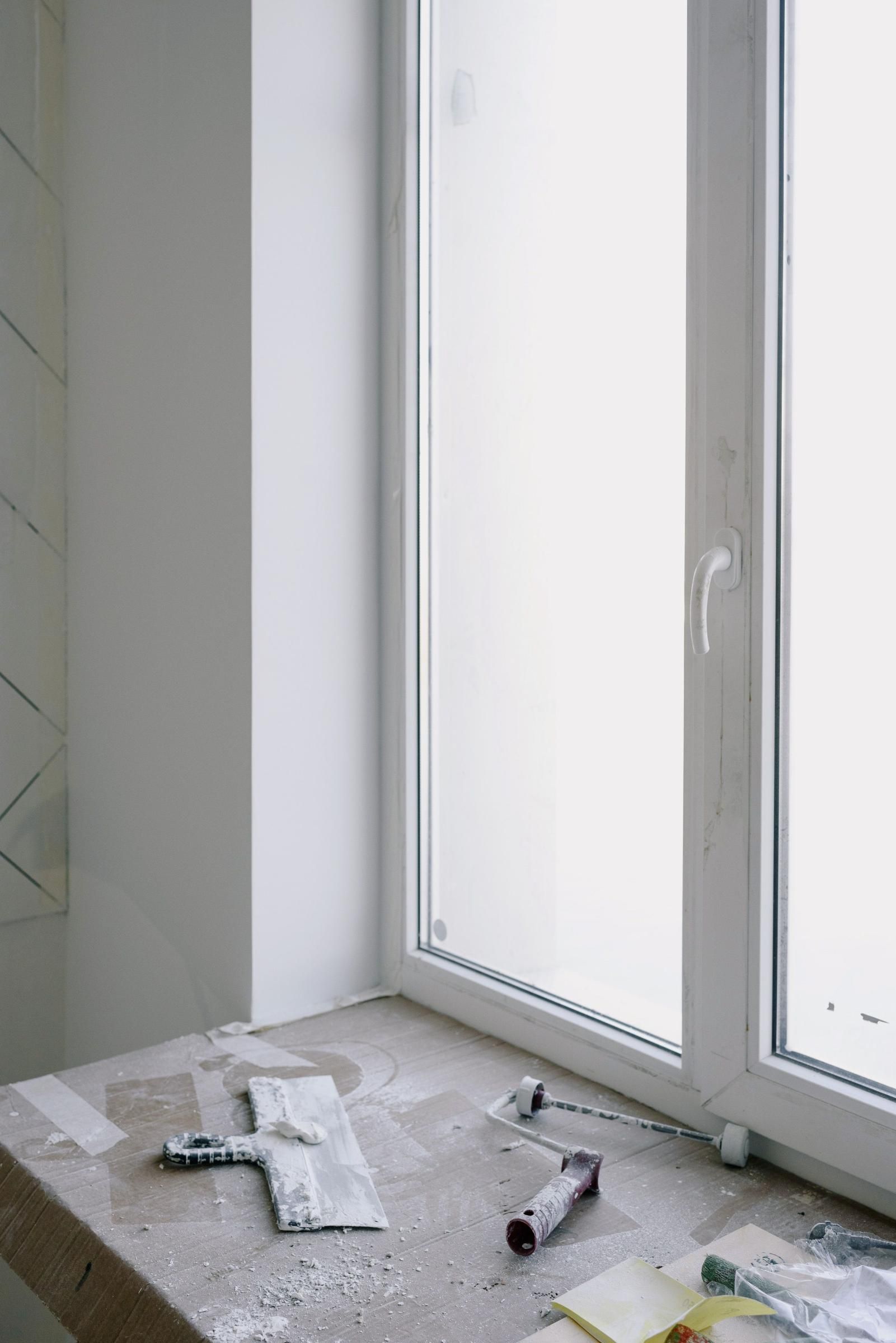 Bathroom with white tiled floor, broken items scattered near a window and a sliding glass door.