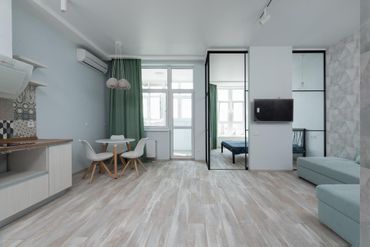 Bright modern studio apartment with kitchenette, dining nook, sofa, and large windows.