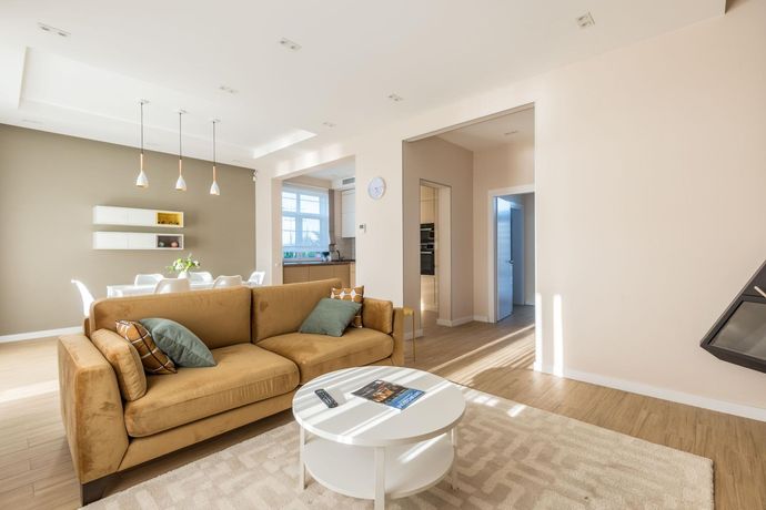 Bright modern living room with tan sofa, white coffee table, rug, and open kitchen area