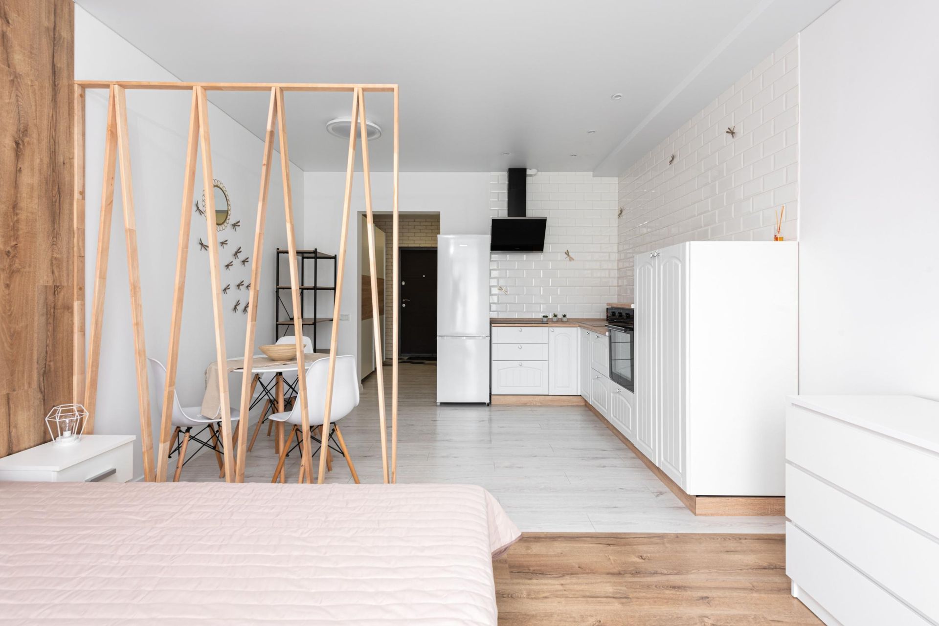 Bright minimalist studio apartment with bed, dining area, kitchenette, and white storage cabinets
