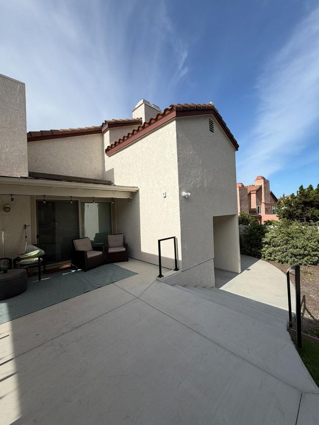 Patio beside a stucco house with covered seating, a walkway, and blue sky above