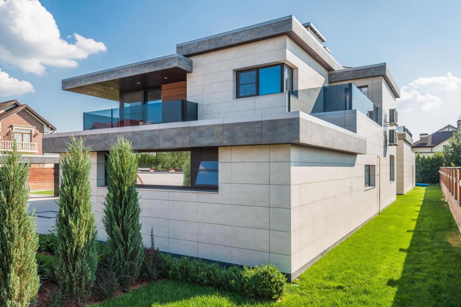 Modern two-story house with gray facade, blue windows, and green lawn under a bright sky