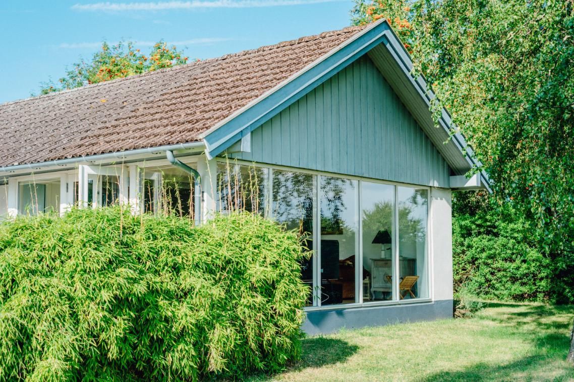 Modern house with large windows, sloped roof, and lush green garden under a blue sky