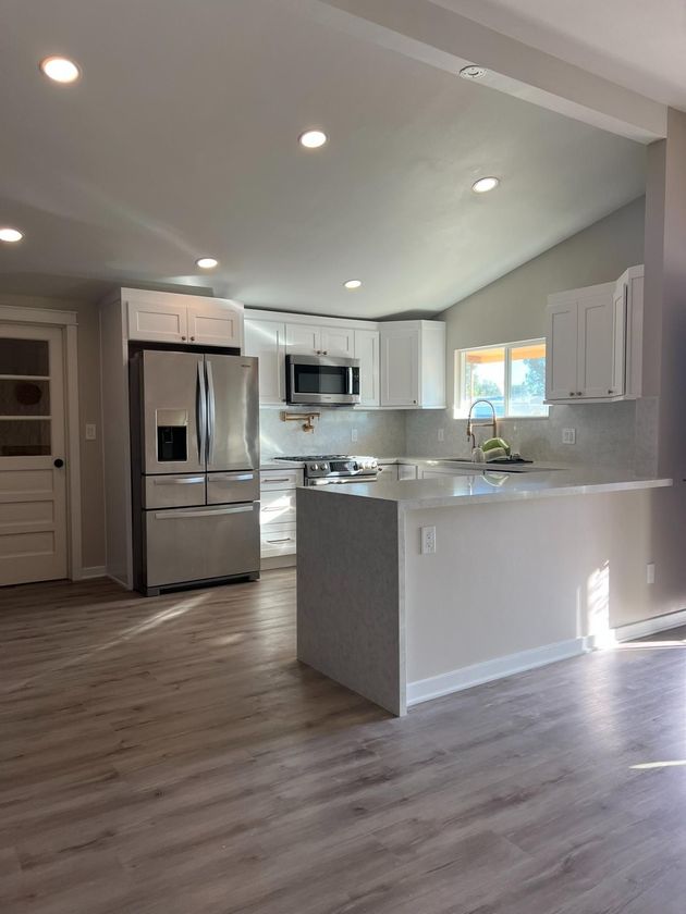 Bright modern kitchen with stainless steel appliances, white cabinets, island, and gray wood-look floors.