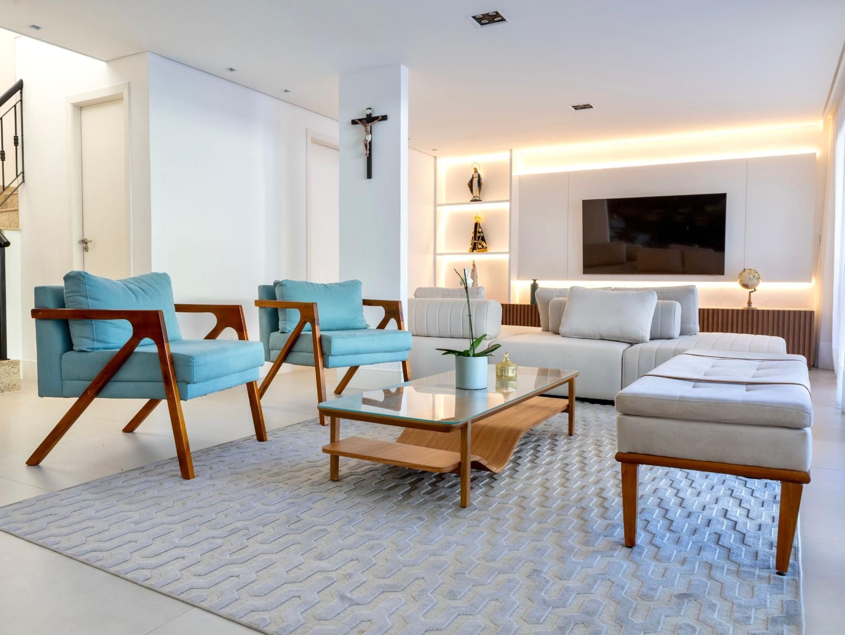 Modern living room with blue chairs, white sectional sofa, glass coffee table, and TV on a lit wall unit