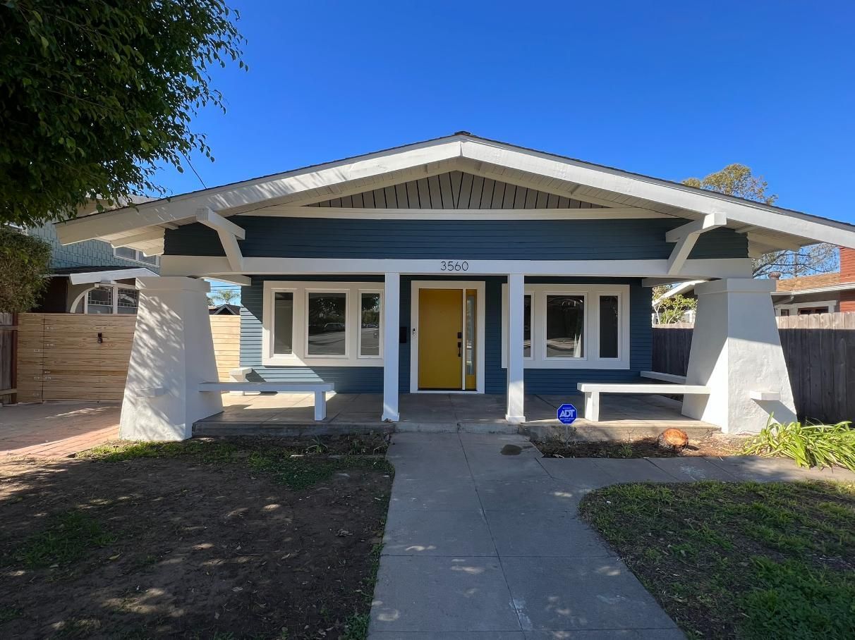 Front view of a blue house with white trim, yellow front door, and a concrete walkway